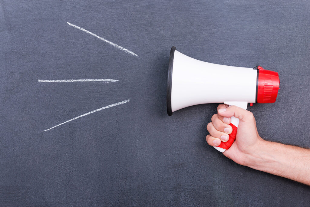 Megaphone . Close-up of human hand holding megaphone against blackboard