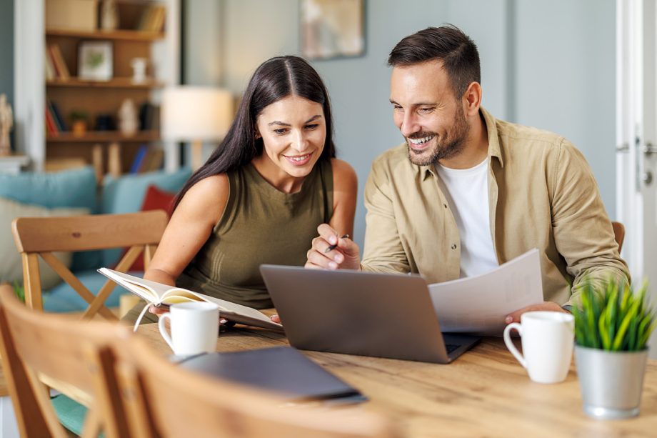 Married couple sit at a table in the living room with laptop,working from home office. Online meeting.